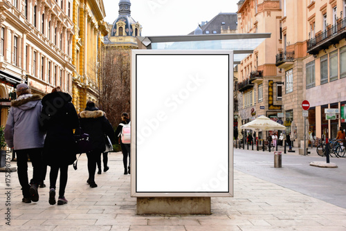bus shelter at busstop. white poster ad display space and lightbox. mockup template. blank ad panel. glass design. urban street setting with storefronts. soft background with people's silhouettes