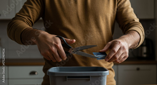 Person cutting credit card over trash bin, symbolizing financial decisions, debt management, or impact of inflation on consumer spending. scene is set in home environment