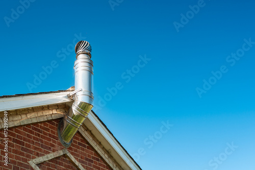 Shiny metal aluminium flue and rotating cover attached to a new central heating system. The large pipe extends to the gas fired heating system.