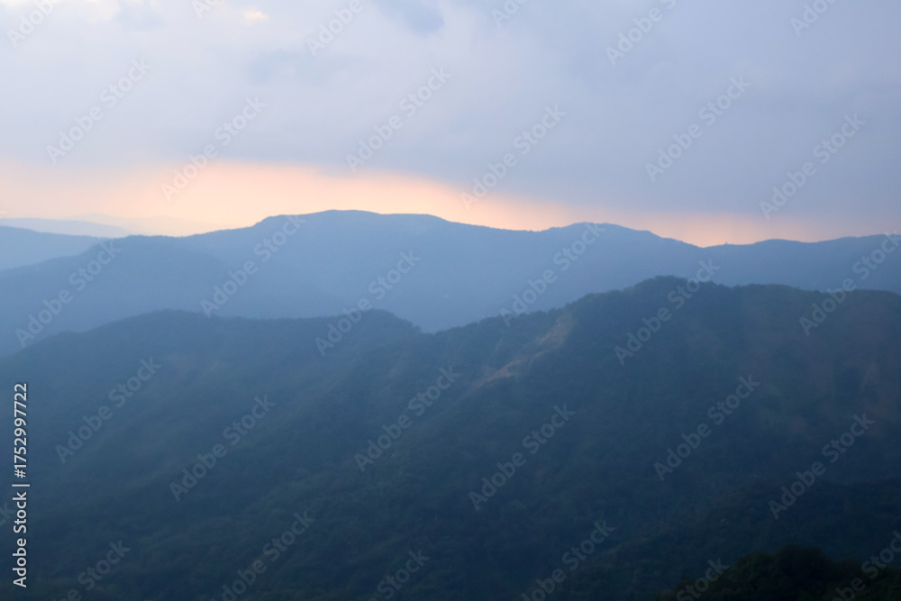 Naklejka premium Calm Kerala mountains at sunset, blue-toned hill layers in soft light and haze, evoking peaceful wilderness and travel inspiration