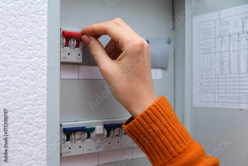 Woman hand turning on a red circuit breaker switch in an electrical panel. Home fuse box for electricity control and safety concept.