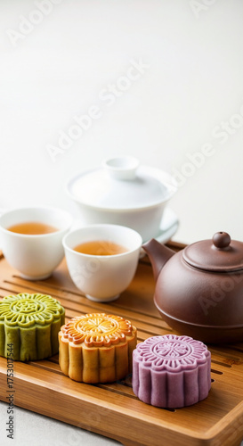 Colorful traditional mooncakes with a Chinese tea set on a wooden tray. Mid-Autumn Festival dessert and pastry. Asian holiday food culture concept on a white background