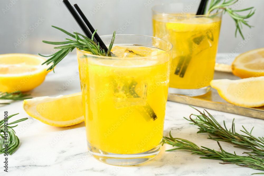 Fototapeta premium Glasses of tasty cocktails with lemon and rosemary on white marble table, closeup