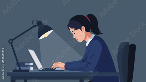 A young woman wearing a dark blue blazer, is working on her laptop at a desk.