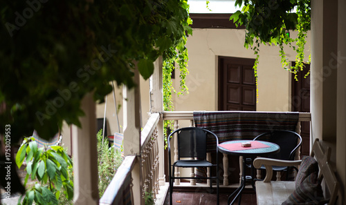 A cozy balcony in Tbilisi, Georgia, with a small table and chairs and lush greenery. The wooden railings and traditional design evoke a sense of warmth and comfort, enhanced by the soft, natural light