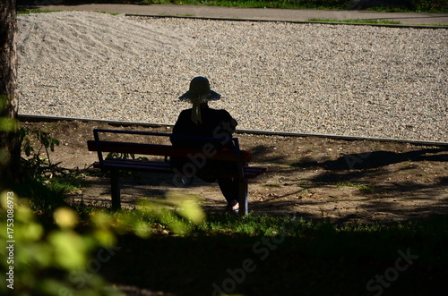 silhouette of a lady in a hat on a bench under the shade of foliage in a park