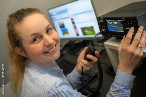 Young smiling woman with ribbon in her hair operating amateur radio on shortwave, holding a microphone and representing YLs and females in STEM and technology fields