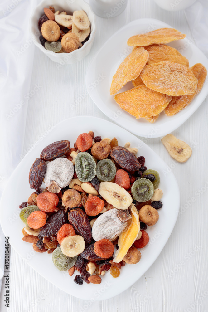 Fototapeta premium Mix of dried tropical fruits, nuts, and raisins on a white table.