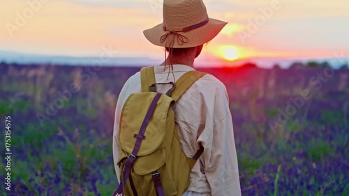 A girl tourist with a hat and a backpack walks through a lavender field during a beautiful sunset in Provence, France
