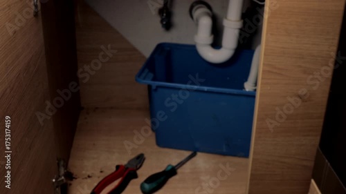 tools and bucket arranged under kitchen sink ready for plumbing repair work, close up of organized equipment and pipes in cabinet space, concept of home maintenance, repair service, plumbing industry