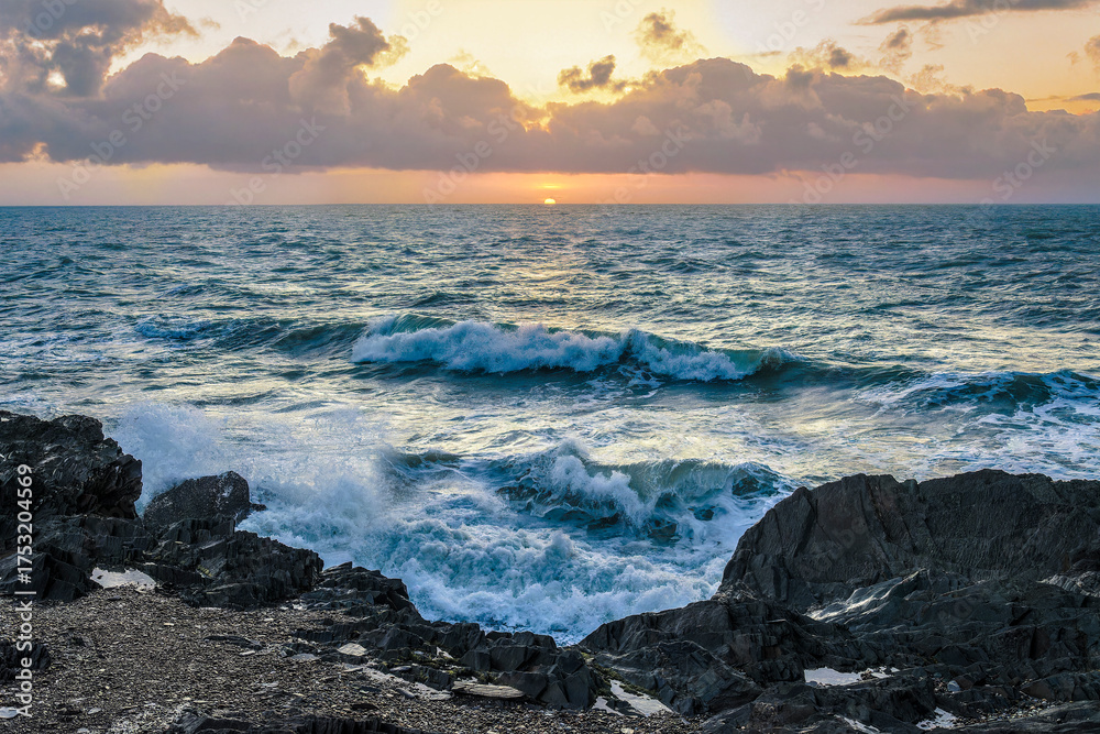 Obraz premium Golden sunrise over the Irish coast, waves crashing on dark rocks, dramatic sky with warm light reflection.