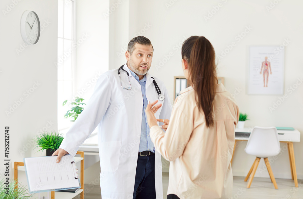 Fototapeta premium Portrait of male doctor arguing with frustrated young woman patient standing in medical clinic. Man physician talking with female patient dissatisfied with treatment in office. Medicine concept.