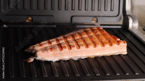 Salmon fillet grills on electric grill with grill marks. Fish cooks slowly and releases steam. Grilled salmon shows healthy food and clean eating.