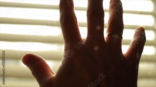 Silhouetted Hand Blocking Sunlight Through Blinds