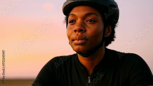 Confident cyclist in black sportswear and helmet pauses outdoors at sunset, enjoying a peaceful evening ride in tranquil surroundings