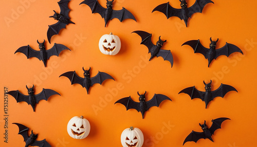 Motivo a tema Halloween composto da pipistrelli neri di plastica e mini-zucche bianche sorridenti disposti su uno sfondo arancione brillante.