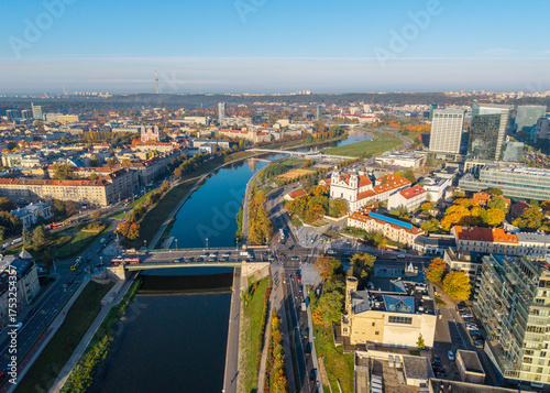 Aerial drone view of Vilnius city center, Lithuania, during autumn sunrise. The St. Raphael Church stand among new skyscrapers and historic districts.