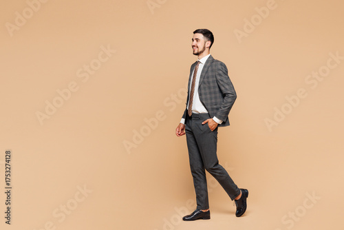 Full body side profile view young fun successful employee business man corporate lawyer wear classic formal grey suit shirt tie work in office walking going isolated on plain beige background studio