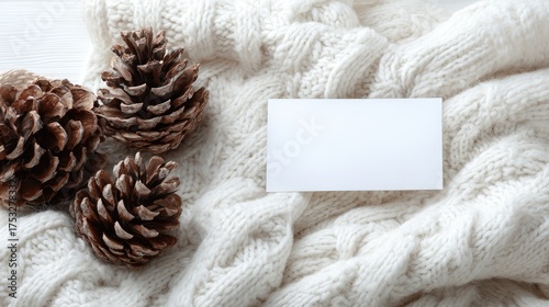 Pine cones rest on a cozy white knitted blanket with a blank card.