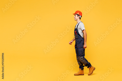 Φωτογραφία Full body side profile view young happy employee laborer handyman man wear helmet overall walk go isolated on plain yellow background