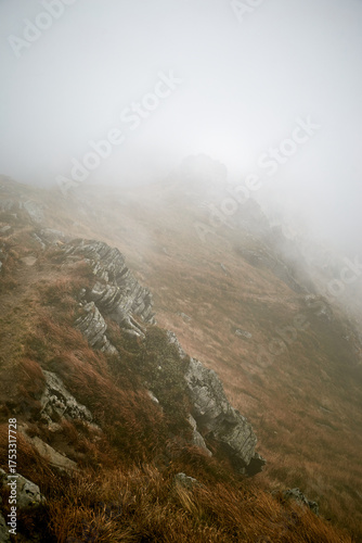 Mist-covered mountain trail winding through rugged terrain on a foggy day. Autumn hiking in Carpathian Mountains, Ukraine
