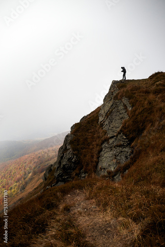 Hiker stands on rocky outcrop overlooking misty mountain landscape in autumn. Autumn hiking in Carpathian Mountains, Ukraine