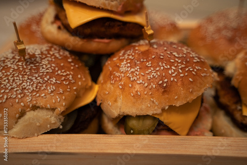 Homemade cheeseburgers on a wooden tray. A custom homemade dish. Large meat patties with buns sprinkled with sesame seeds. Slightly greedy. Burgers in close-up.