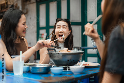Group of asian friends eating noodles together at a street food market, using chopsticks and enjoying a delicious meal in a lively outdoor setting showing culture and lifestyle