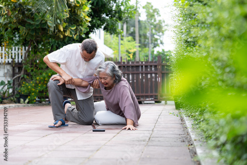 An elderly woman sits on the ground after a fall, assisted by a concerned older man in a quiet outdoor setting. The scene highlights senior vulnerability, caregiving, and the importance of safety.