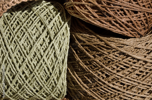 A close-up of large spools of brown and olive green raffia lying in a crocheted brown bag.