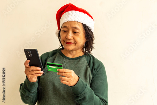 A woman in a green sweater is using a credit card and a cell phone to make a transaction.