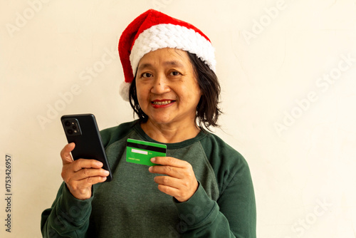 A woman in a green sweater is using a credit card and a cell phone to make a transaction.