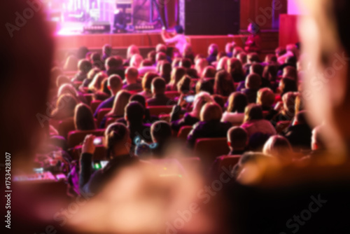 a large audience crowd seated in a majestic theater, theatre, auditorium. the people blurred to highlight the stage or screen for a show, concert, or film festival
