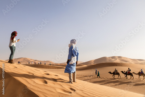 Tourists exploring Sahara dunes with camels in Morocco