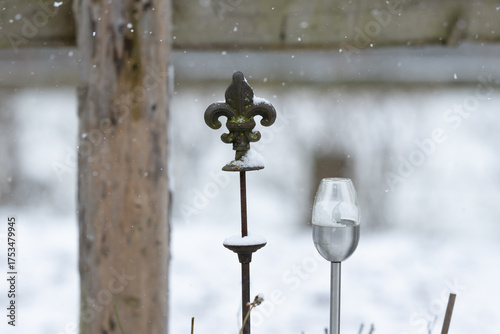 ein Ornament aus Gusseisen neben einer elektrischen solar Fackel Detailaufnahme close-up im Winter im Schnee vor einem Zaun aus Lärchenholz