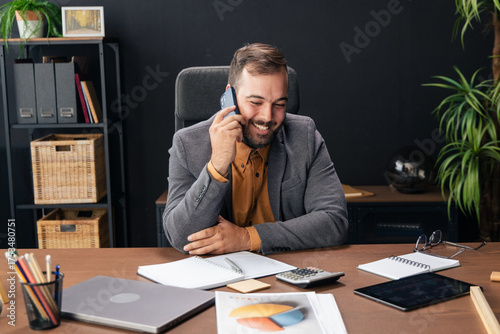 Businessman smiling while talking on a mobile phone at his office desk