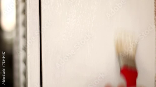 A man paints an old cabinet with a brush. He holds a red brush in his hand against the background of an old white cabinet.