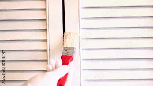 A man paints an old cabinet with a brush. He holds a red brush in his hand against the background of an old white cabinet.