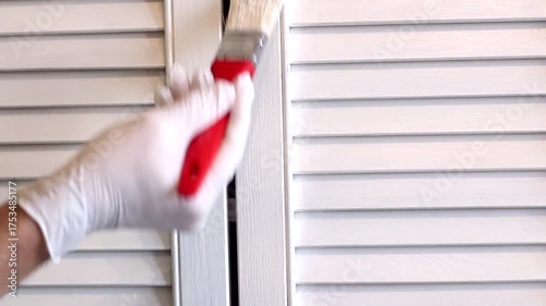A man paints an old cabinet with a brush. He holds a red brush in his hand against the background of an old white cabinet.