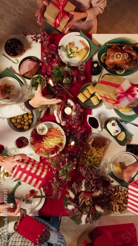 Friends giving presents to each other top view, celebrating new year, sitting at dining table. International young people making surprises. Diverse students during christmas party at home. 