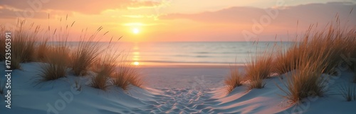 Photo features a beach at sunset. Golden sun sets over sea. Sand dunes with grass in foreground. Calm water reflects the colors creating peaceful mood.