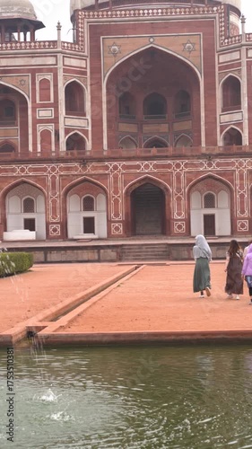 Panning shot showing the fountains and gardens of Humayun's tomb in delhi with people walking to the central dome structure with arches a popular mughal monument