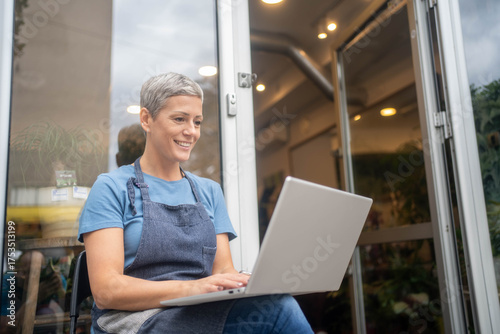 Smiling confident female florist using laptop to receive online flower orders while running her small business shop