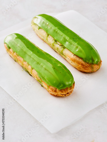 Two well-made green eclairs sit on a white surface. The glossy glaze adds a vibrant touch, making them look very appetizing and perfect for dessert lovers