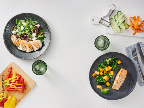 Two beautifully arranged plates of food feature grilled salmon and chicken alongside colorful vegetables. Fresh greens and sliced cucumbers are included for a healthy meal experience