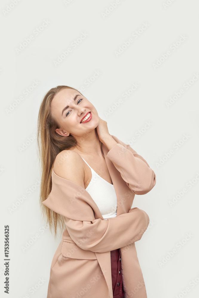 Fototapeta premium Young caucasian female smiling in beige coat with white top against light background.