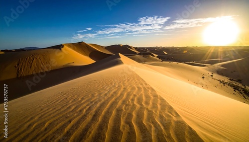 Fototapeta Naklejka Na Ścianę i Meble -  The sun sets over rolling, rippled sand dunes in a vast desert landscape