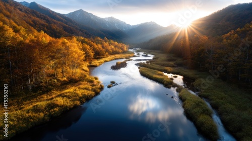 The autumn foliage along a winding river reflects the stunning mountains in the background, creating a harmonious blend of warm colors under a beautiful sunset sky.