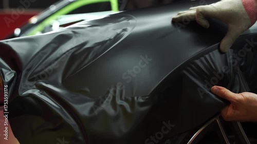 Matte black vinyl wrapping around car with smooth alignment over curves and edges 4k video. Matte black vinyl wrap application on front fender and wheel arch of luxury vehicle. Vinyl Wrapping of Car.