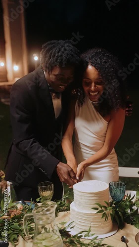 The bride and groom cut the wedding cake and feed each other in turn at the outdoor wedding party at night